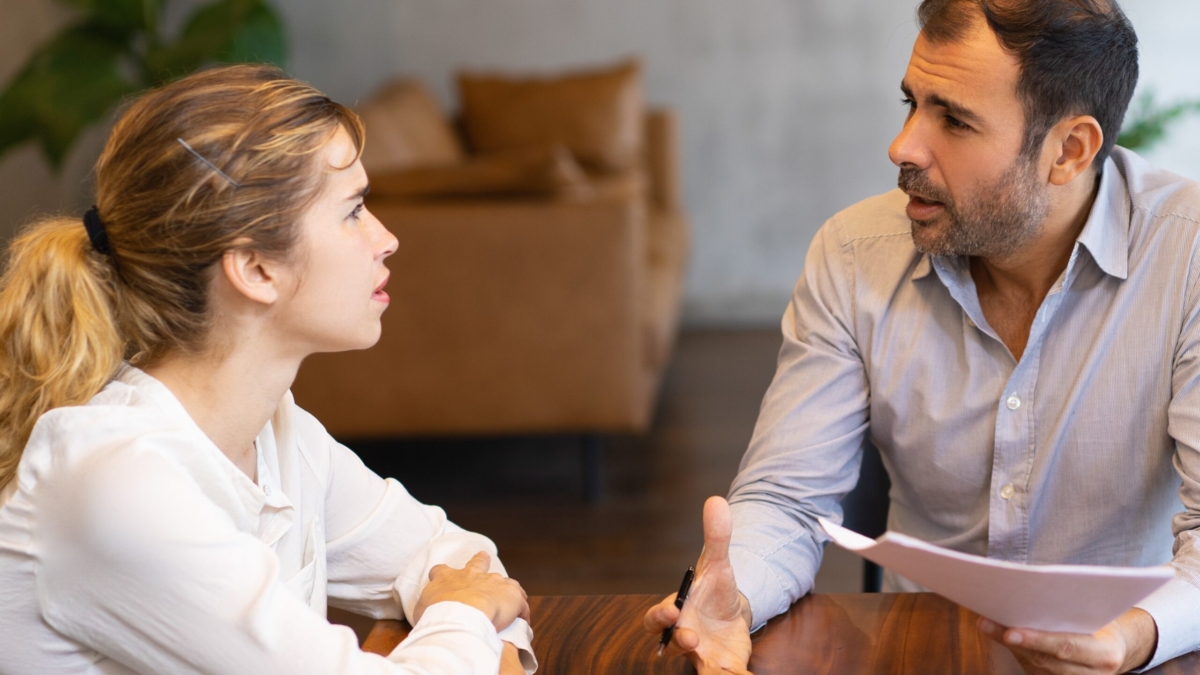 Intern and mentor discussing job specific. Latin man in shirt explaining paper details to young blonde colleague. Mentorship concept