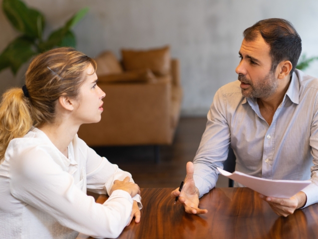 Intern and mentor discussing job specific. Latin man in shirt explaining paper details to young blonde colleague. Mentorship concept
