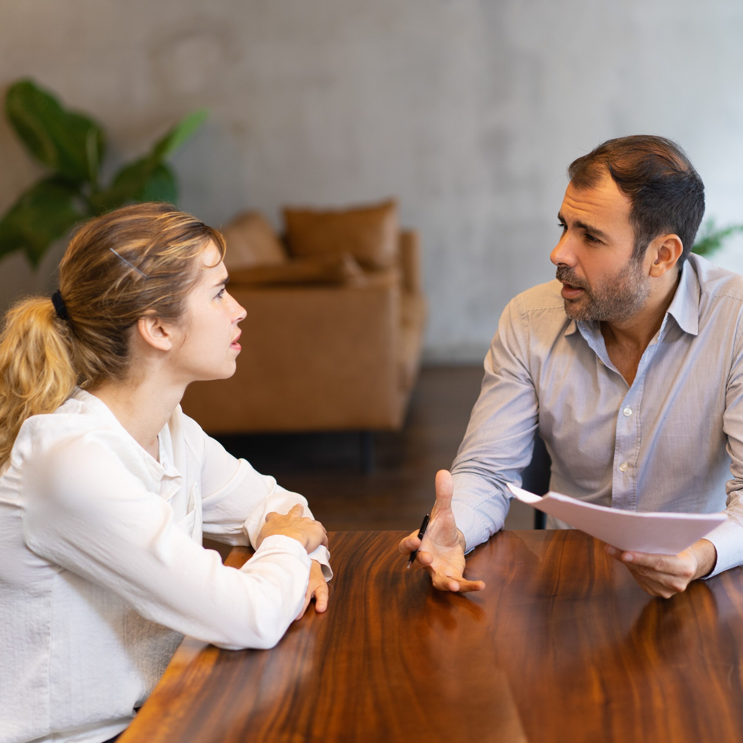 Intern and mentor discussing job specific. Latin man in shirt explaining paper details to young blonde colleague. Mentorship concept